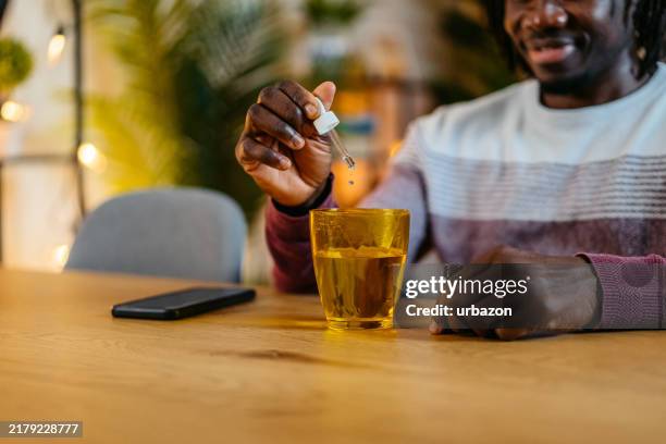 joven poniendo gotas de medicina en un vaso de agua en casa por la noche - botella con gotero fotografías e imágenes de stock