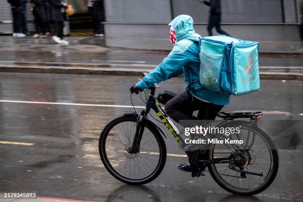 Deliveroo takeaway delivery cycle courier in heavy rain on 8th October 2024 in London, United Kingdom. Deliveroo acts as an intermediary between...