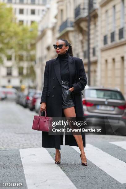 Emilie Jospeh wears a wool, extra Long, tailored double breasted black coat from COS, black high-waisted leather cargo shorts, black fitted...