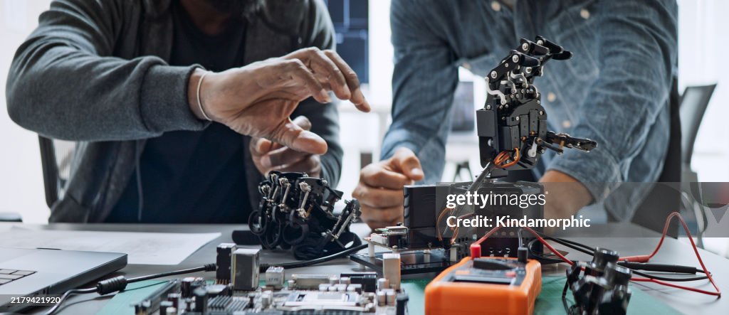 Black and white male software developer programmers work together on robot hand machine coding, use computer control robotic arm circuit. Programming language, hardware development technology concept