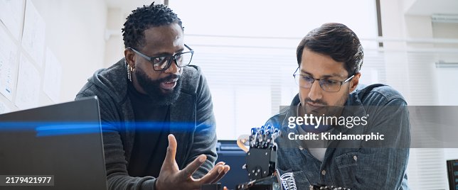 Black and white male software developer programmers work together on robot hand machine coding, use computer control robotic arm circuit. Programming language, hardware development technology concept Black and white male software developer programmers work together on robot hand machine coding, use computer control robotic arm circuit. Programming language, hardware development technology concept
