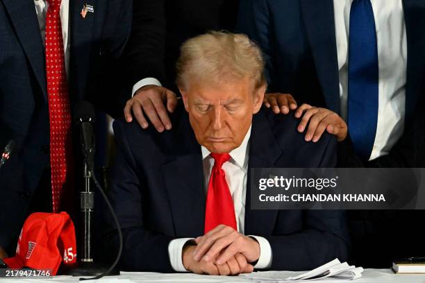 Former US President and Republican presidential candidate Donald Trump prays during a roundtable discussion with Latino community leaders at Trump...
