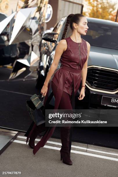 Guest wears burgundy leather skirt and top, long burgundy tights, boots and green bag during the 10th season of the Visa Fashion Week Almaty on...