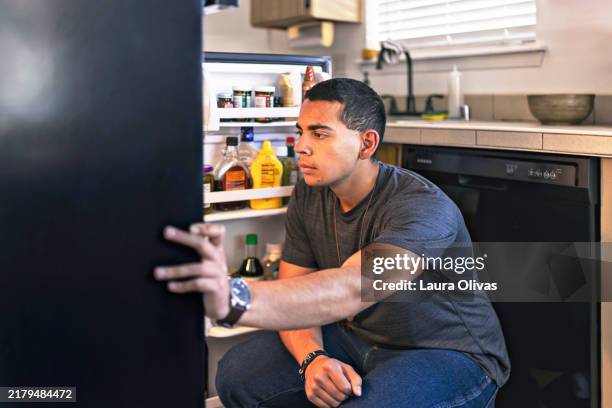 young man looking in his refrigerator - open fridge man stock pictures, royalty-free photos & images