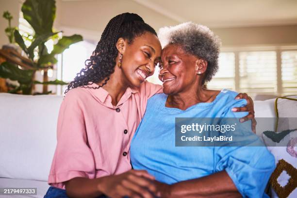 cheerful young woman hugging grandmother on sofa at home - granddaughter stock pictures, royalty-free photos & images