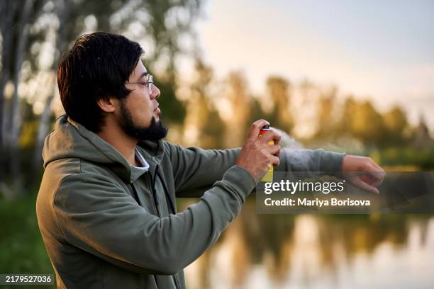 a adult man sprays himself with mosquito and midge repellent. - insect repellant stock pictures, royalty-free photos & images