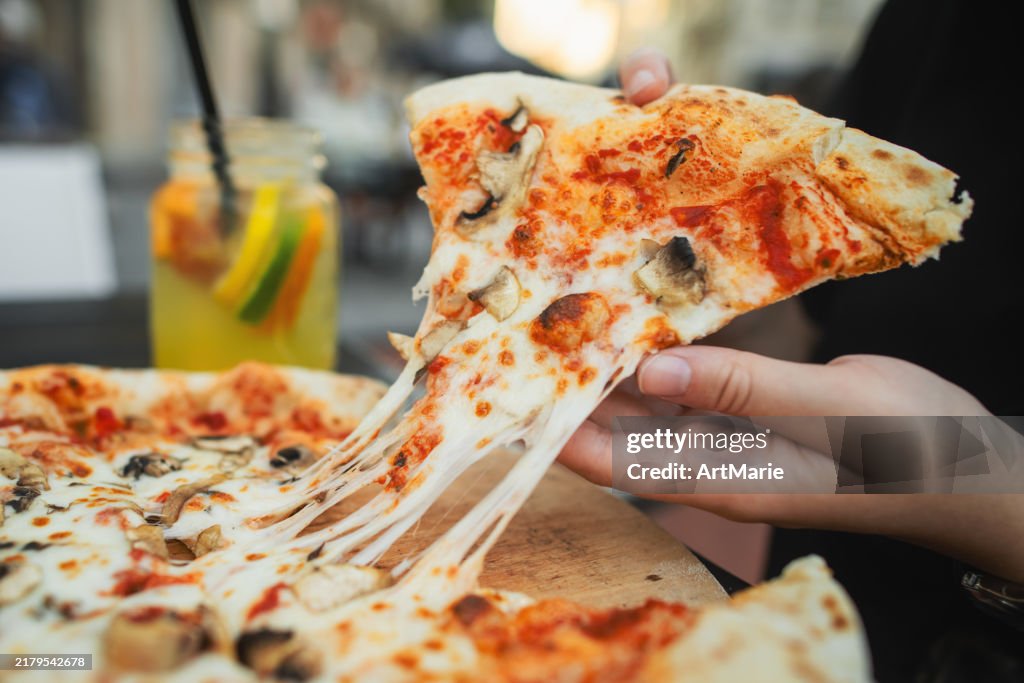 Mains prenant une part de délicieuse pizza aux champignons et étirant le fromage dans un restaurant pizzeria
