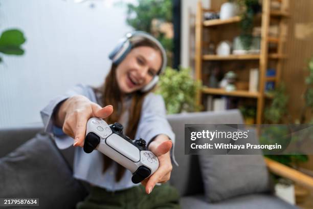 young woman enjoying video game with controller and headphones - brand name video game photos et images de collection