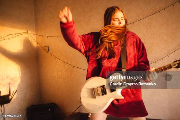 young woman playing electric guitar standing on the bed at home - chitarra elettrica foto e immagini stock