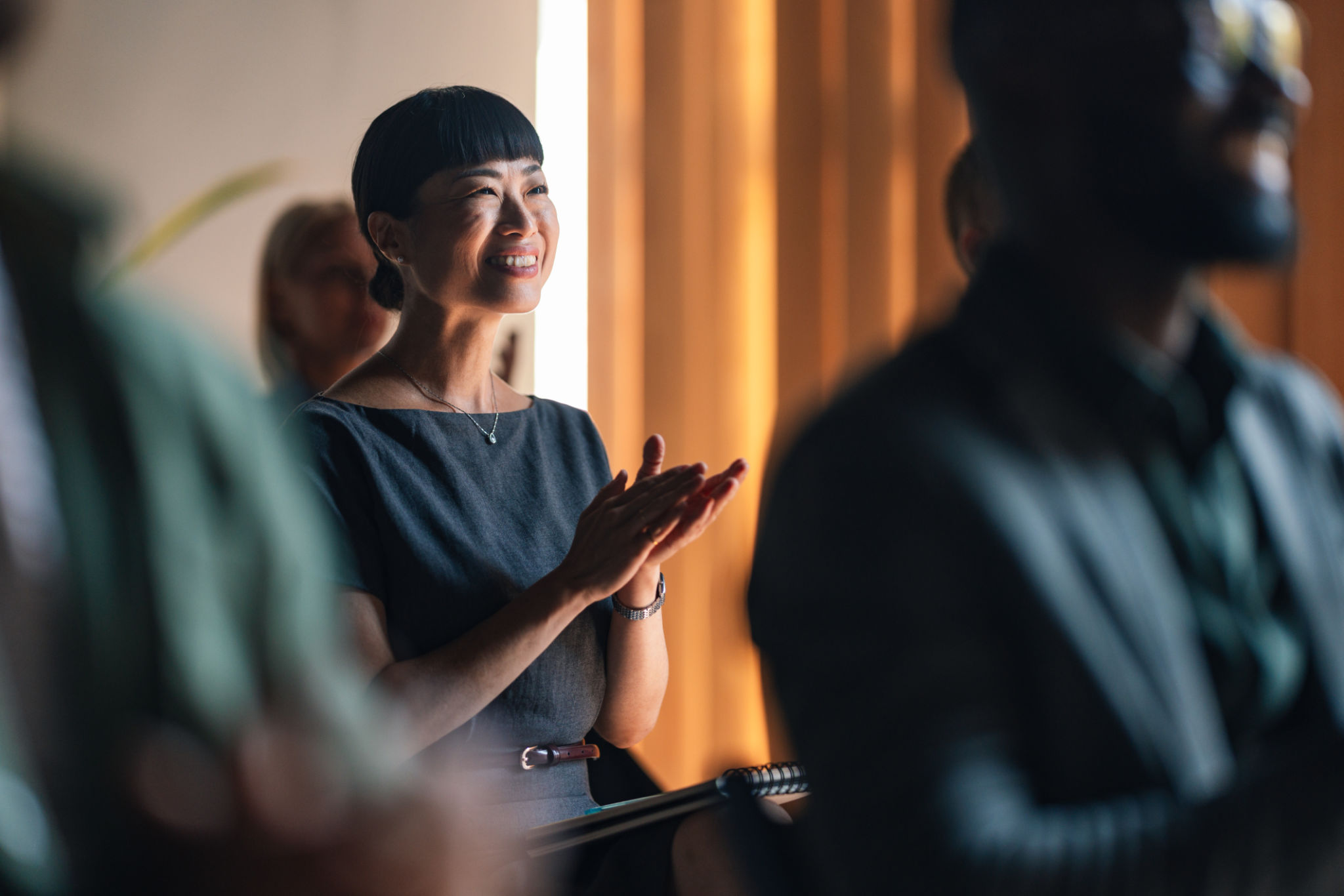 A business professional applauds enthusiastically during a lively conference session. The scene captures engagement, networking, and positive emotion, highlighting the success of the corporate event.