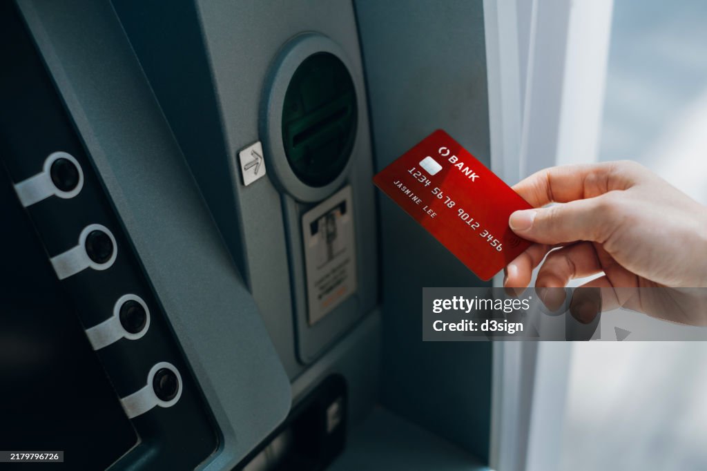 Female hand inserting bank card into automatic cash machine (ATM) to access bank account services in the city. Cash withdrawing, paying bills, checking account balance, transferring money. Privacy protection. Mobile banking security. Self-service concept