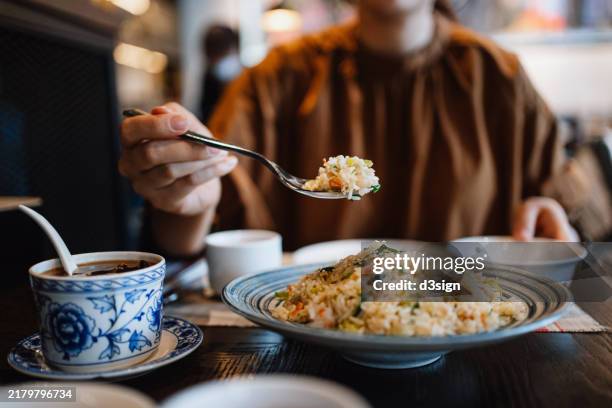 mid-section of young asian woman eating authentic chinese fried rice while dining in restaurant. enjoying traditional chinese cuisine and food culture. people, food and lifestyle - fried rice stock pictures, royalty-free photos & images
