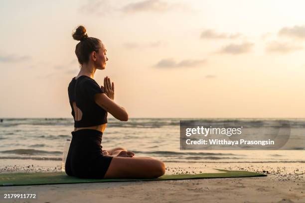 woman practicing yoga on beach at sunset meditation - pose-alternative photos et images de collection