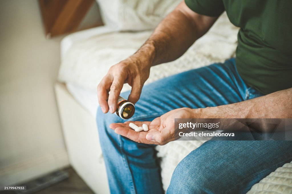 Reifer erwachsener Mann im gemütlichen Interieur des Schlafzimmers ( Einnahme von Medikamenten)