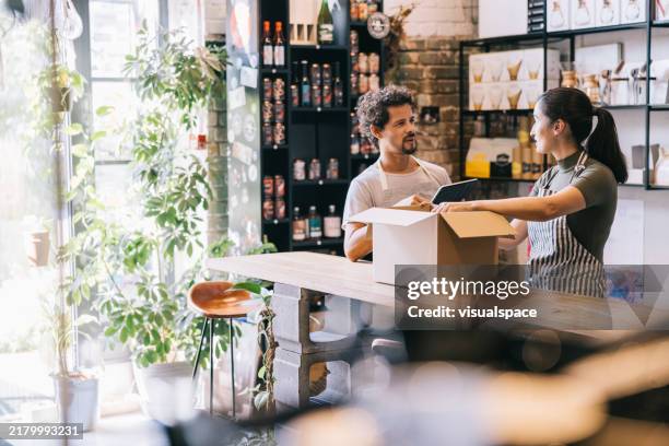 de pie en el mostrador, la propietaria entabla una animada discusión con su colega mientras prepara un pedido en línea - pequeña empresa fotografías e imágenes de stock