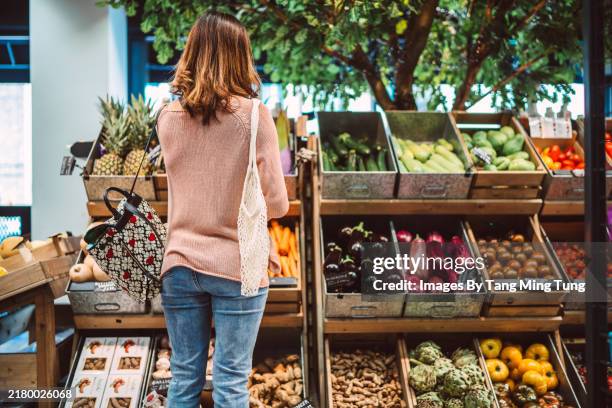 woman shopping for fresh organic produce in a local grocery store - groceries stock pictures, royalty-free photos & images