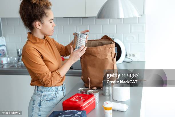 woman organizing emergency supplies in the kitchen for preparedness - gevaar stockfoto's en -beelden