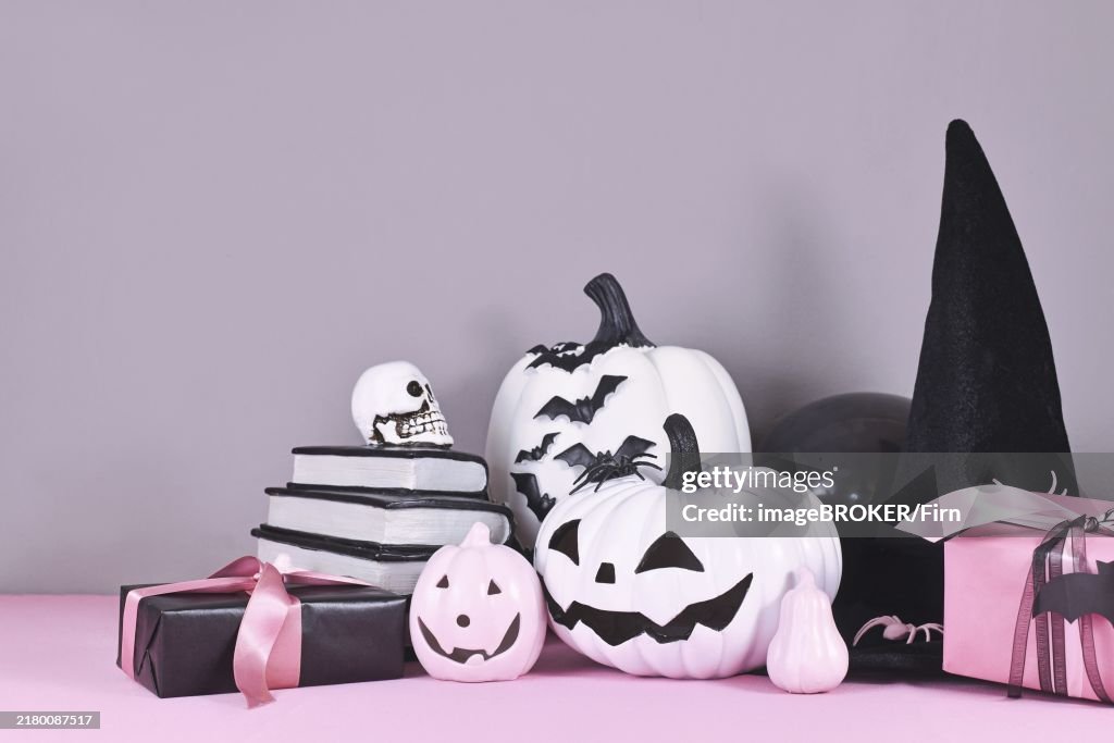 Pink and white Halloween decor with black and white pumpkins, witch hat and spell books on gray background
