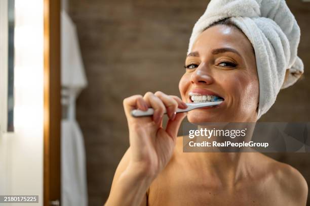 donna in asciugamano che si lava i denti con piacere, all'interno. - lavarsi i denti foto e immagini stock