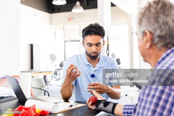 young adult male therapist gestures while helping his male client - ergotherapie stockfoto's en -beelden