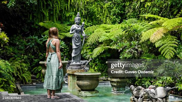 woman admiring guan yin statue in lush garden at gwk cultural park, bali - bodhisattva stock pictures, royalty-free photos & images