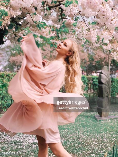 hermosa mujer en vestido impresionante rosa bajo el árbol de flores - vestido rosa fotografías e imágenes de stock