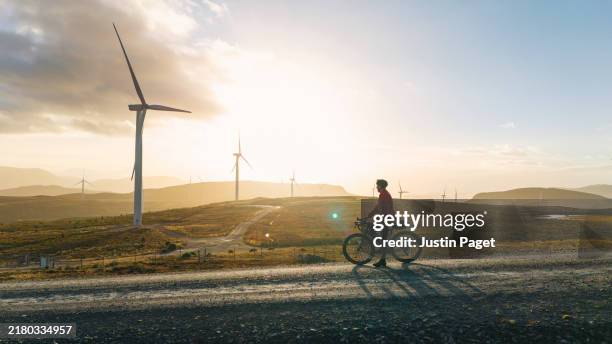side view of a mature cyclist taking in the view of the wind turbines in the mountains in the scottish highlands - energía renovable fotografías e imágenes de stock
