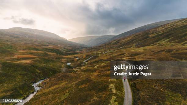 wide landscape shot of a cyclist on a gravel trail in the mountains in the cairngorms - endurance stock pictures, royalty-free photos & images