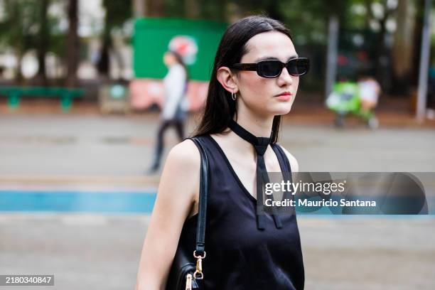 Guest wears black sleeveless top, black choker, white pants, black sunglasses, black shoulder bag at Sao Paulo Fashion Week 2024 N58 - Street Style...