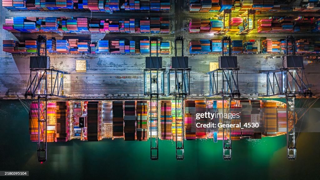 Aerial top view cranes loading containers at night time.