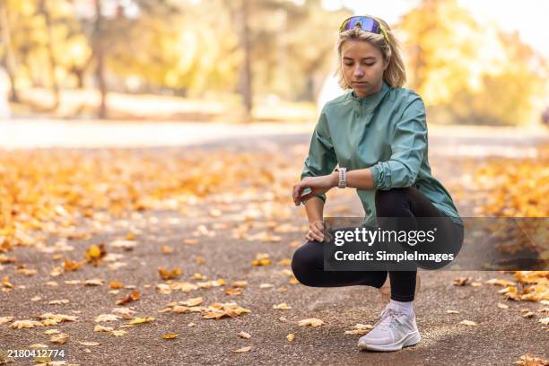 portrait of a blonde athlete checking her sports performance on a smart watch in park. - fitness tracker stock-fotos und bilder