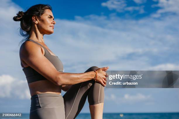 mid-adult woman stretching on the beach in barcelona in spain - strekken stockfoto's en -beelden