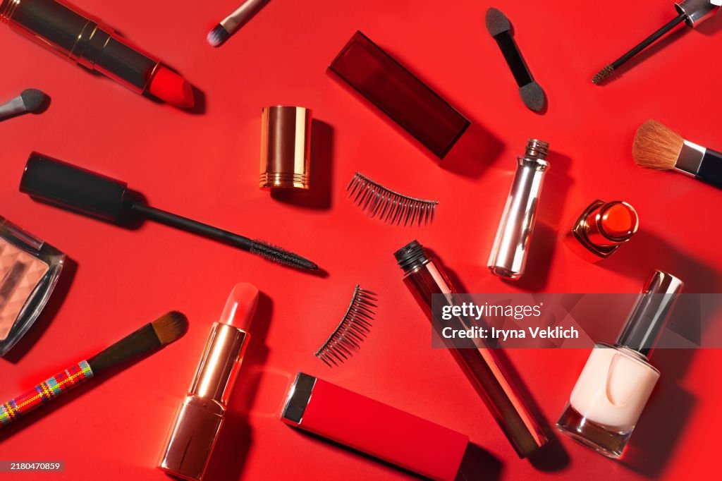 Set of Beauty Products Laid Out on a Red Color Background. Cosmetic Make-up Products for a woman Make-Up Brushes, Red Lipstick, Mascara, Eye Mascara Applicator, Beige Nail Polish, Face Powder Blush Palette, False Eyelashes, eyebrow mascara, Lip Gloss.