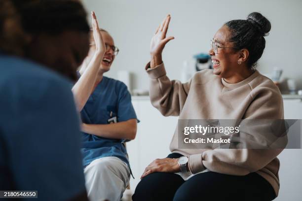 happy female patient giving high-five to medical worker sitting at hospital - boa notícia imagens e fotografias de stock