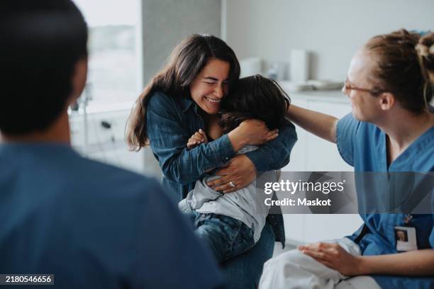 happy woman embracing son after receiving good news at healthcare center - boa notícia imagens e fotografias de stock