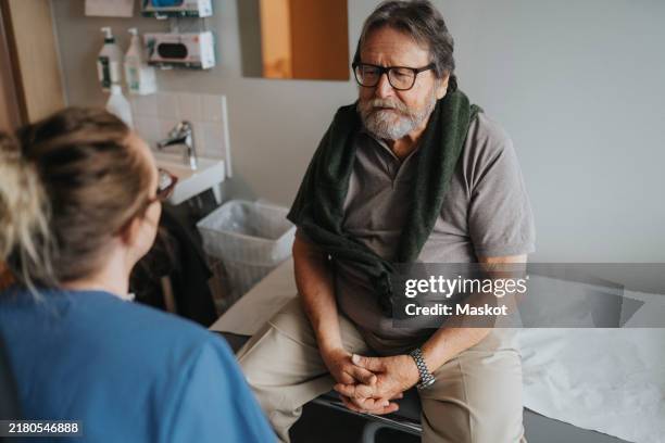 high angle view of senior man discussing with medical worker during visit at hospital - medical examination room stock pictures, royalty-free photos & images