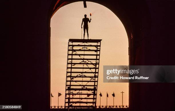 Framed by the entrance to Los Angeles Memorial Coliseum, the silhouette of American Olympian Rafer Johnson is seen holding the Olympic Torch during...