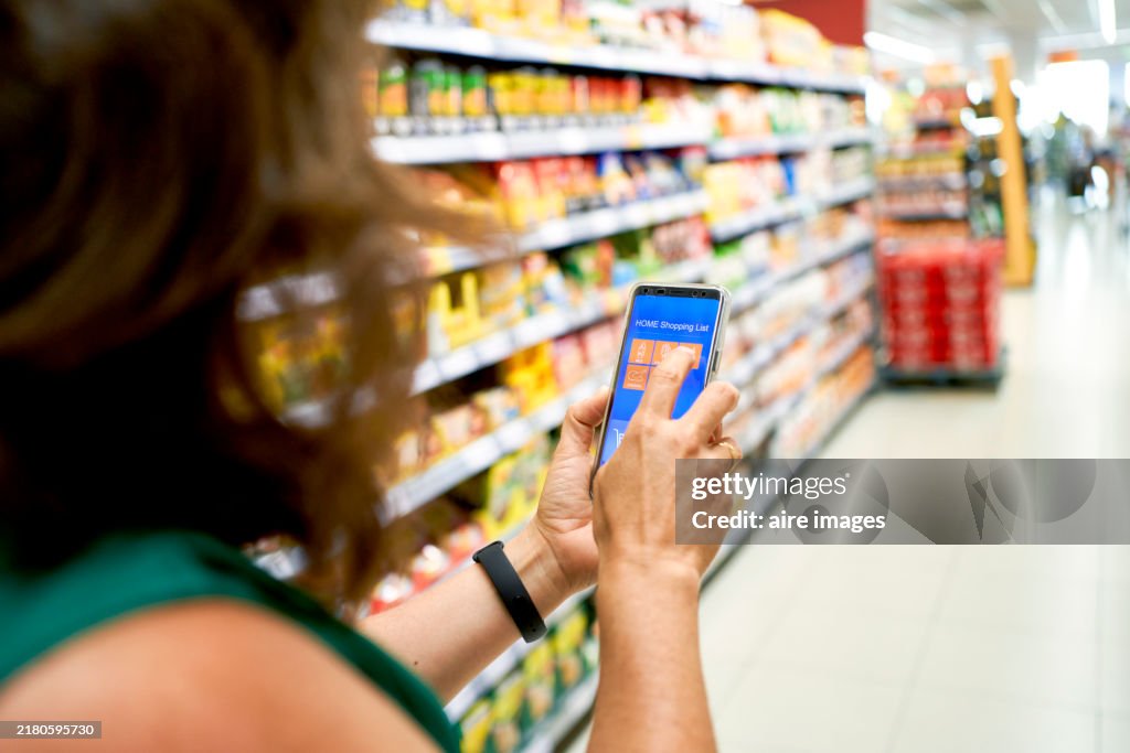 Woman in casual clothes walking through the aisles in a supermarket touching her phone screen side view