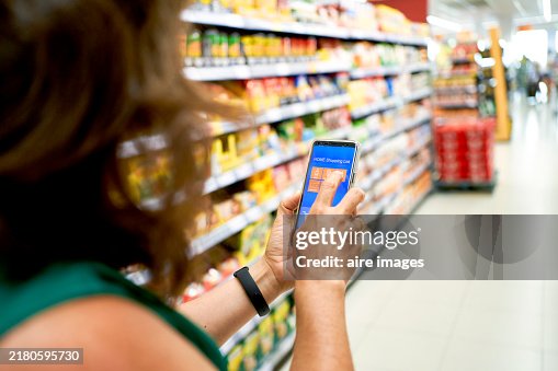 Woman in casual clothes walking through the aisles in a supermarket touching her phone screen side view Woman in casual clothes walking through the aisles in a supermarket touching her phone screen side view