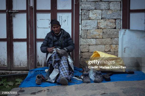 Local Nepali man mends hiking boots on the side of the main street through Namche on October 07, 2024 in Namche Bazaar, Nepal. Trekking in Nepal...