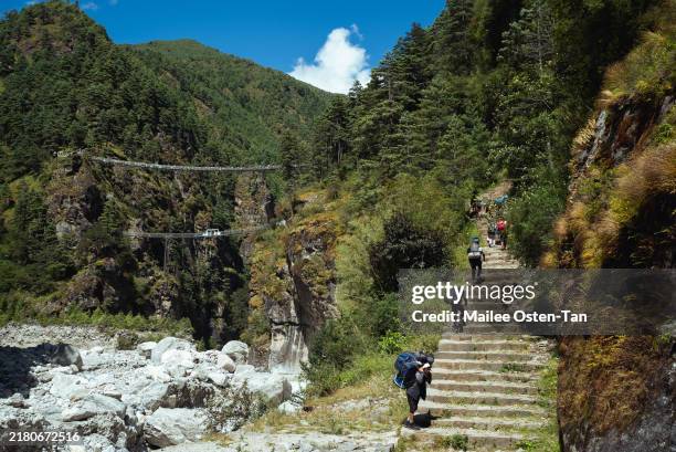 Trekkers and porters climb the stairs that lead up to the Tenzing-Hillary bridge on October 07, 2024 in Namche Bazaar, Nepal. Trekking in Nepal...