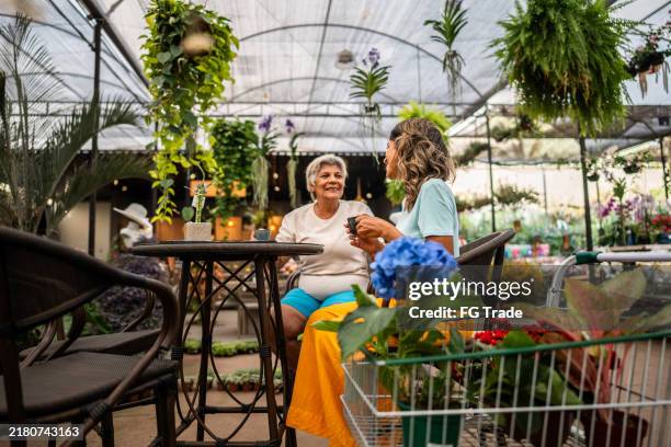 mother and daughter talking and drinking coffee in coffee shop at a garden center - tuincentrum stockfoto's en -beelden
