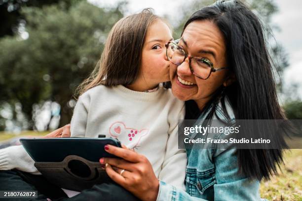 retrato de una niña con síndrome de down besando a su madre al aire libre - discapacidad del desarrollo fotografías e imágenes de stock