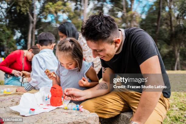 father helping daughter with down syndrome painting a toy with paint outdoors - single father stock pictures, royalty-free photos & images