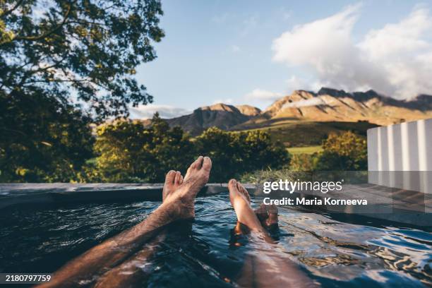 a couple relaxes in an outdoor hot tub overlooking the mountains. - outdoor hot tub stock pictures, royalty-free photos & images