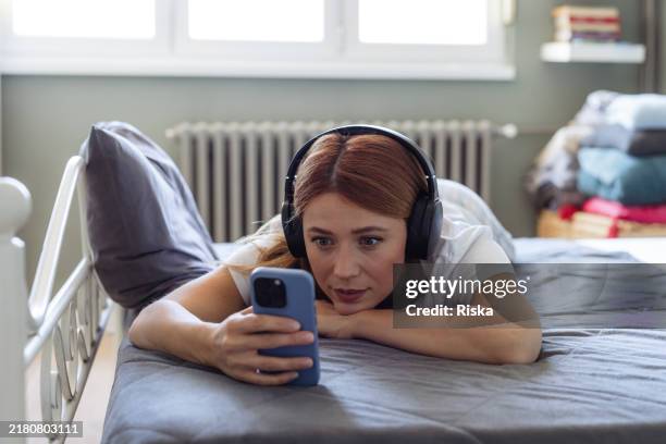 donna che si rilassa a letto e guarda il telefono - video on demand foto e immagini stock