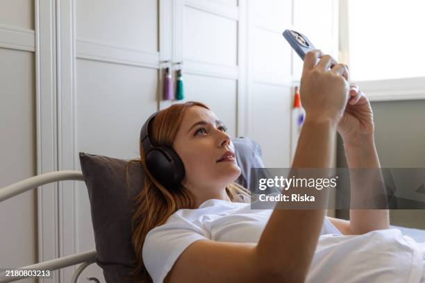 woman relaxing in bed and using phone - muziekstreamingdienst stockfoto's en -beelden