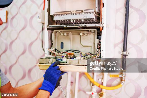 a technician carefully working on the internal components of a wall-mounted boiler. he is using his hands to make adjustments or repairs to the wiring inside the open unit. - broken air conditioner stock pictures, royalty-free photos & images