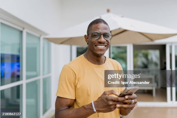 portrait of a man holding smartphone at home - dark skin tone stock pictures, royalty-free photos & images