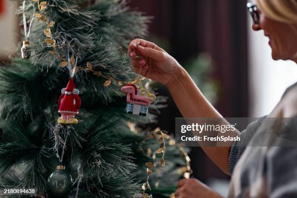 woman decorating a christmas tree with festive ornaments - decorating-the-christmas-tree stock pictures, royalty-free photos & images